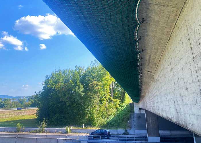 Ein grünes Sicherheitsnetz von Endriagonets ist an einer Brücke befestigt